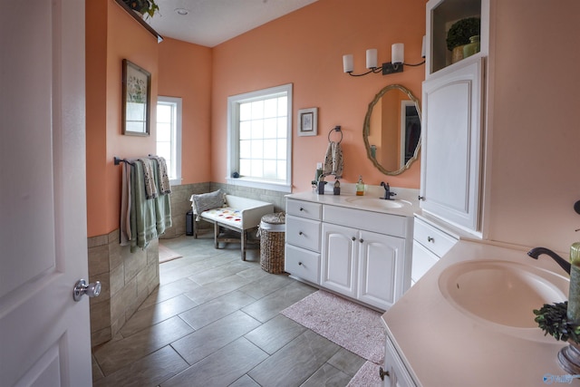 full bath with two vanities, a wainscoted wall, and tile walls