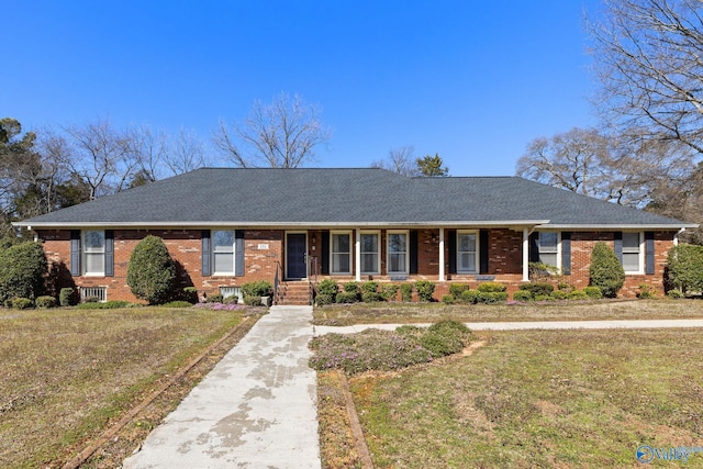 ranch-style home featuring a front yard, a porch, brick siding, and roof with shingles