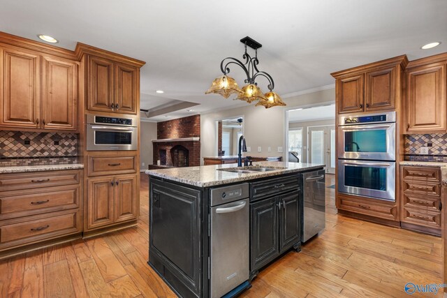 kitchen featuring light wood-type flooring, decorative backsplash, brown cabinets, appliances with stainless steel finishes, and a sink