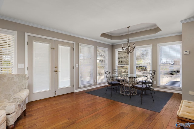 dining area with ornamental molding, a raised ceiling, an inviting chandelier, and hardwood / wood-style floors