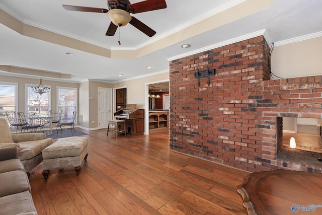 living area featuring baseboards, dark wood finished floors, ornamental molding, ceiling fan with notable chandelier, and a raised ceiling