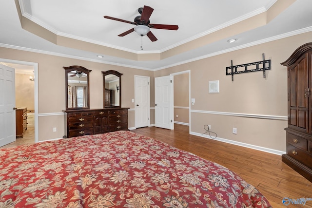 bedroom featuring a tray ceiling, wood finished floors, baseboards, and ornamental molding