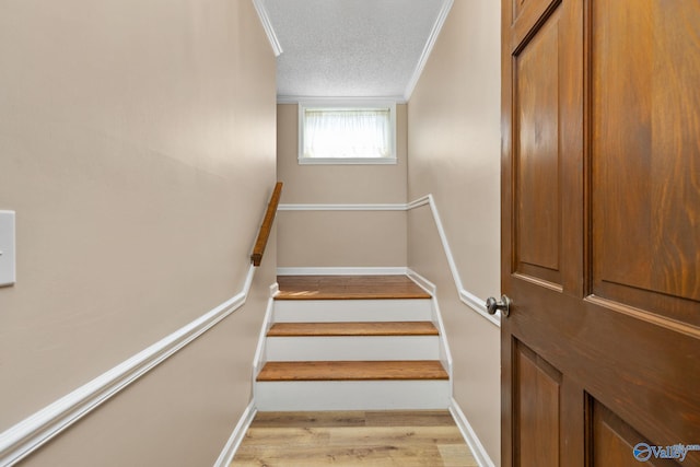 staircase with ornamental molding, wood finished floors, baseboards, and a textured ceiling