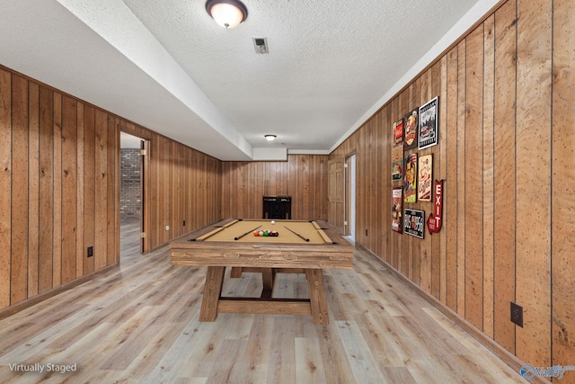 rec room featuring visible vents, a textured ceiling, wood finished floors, and wood walls