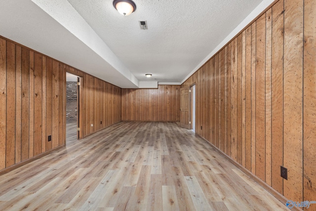 finished below grade area featuring wooden walls, visible vents, light wood-type flooring, and a textured ceiling