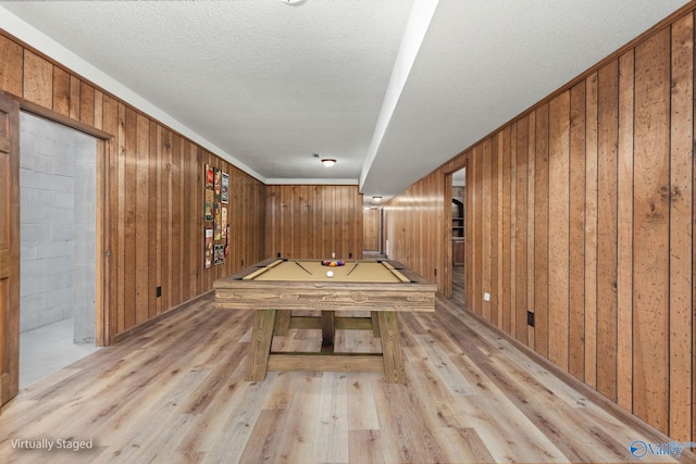 recreation room with pool table, wooden walls, light wood finished floors, and a textured ceiling