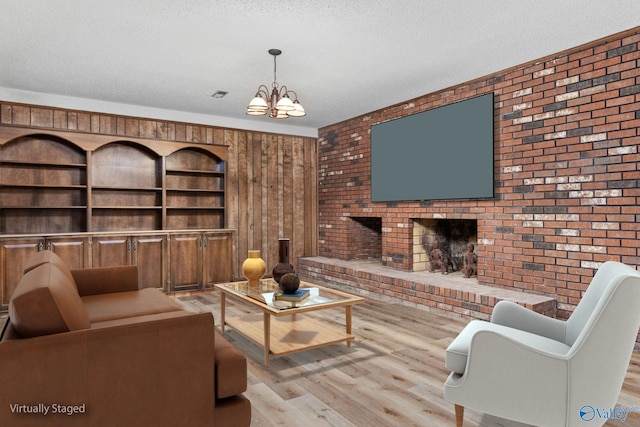 living area with brick wall, a brick fireplace, a chandelier, wood finished floors, and a textured ceiling