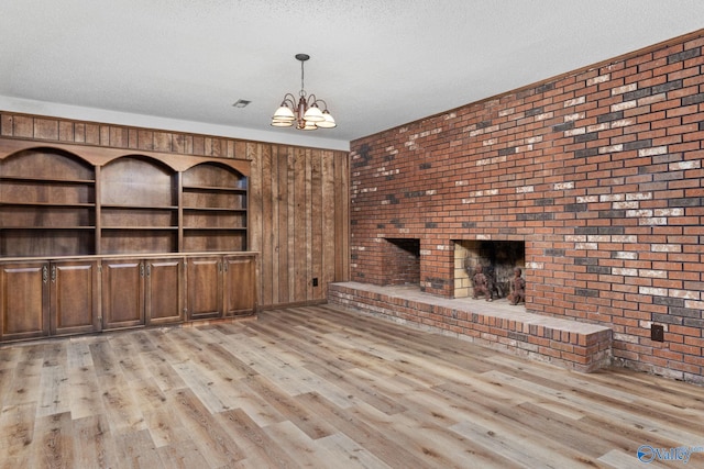 unfurnished living room featuring a notable chandelier, a textured ceiling, a brick fireplace, and light wood finished floors