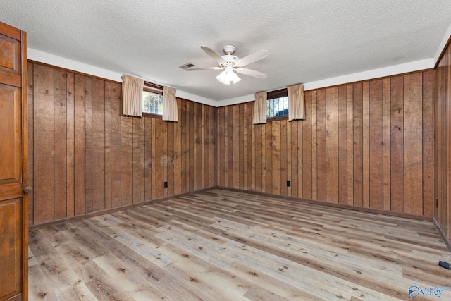 unfurnished room with light wood-style flooring, wooden walls, visible vents, and a textured ceiling