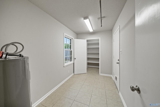 interior space with laundry area, a textured ceiling, baseboards, water heater, and light tile patterned flooring