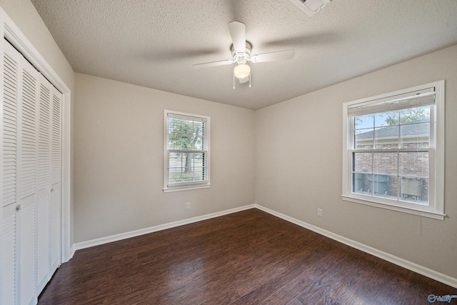 unfurnished bedroom with a closet, dark wood-style flooring, baseboards, and multiple windows