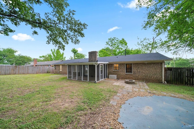 back of property with a chimney, a lawn, a sunroom, a fenced backyard, and an outdoor fire pit