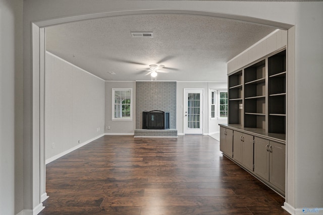 unfurnished living room with crown molding, a textured ceiling, a ceiling fan, visible vents, and dark wood-style floors