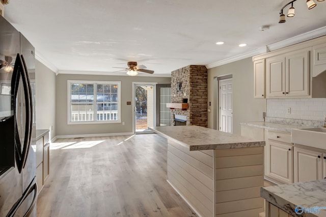 kitchen featuring ceiling fan, a center island, light hardwood / wood-style flooring, stainless steel fridge, and a fireplace