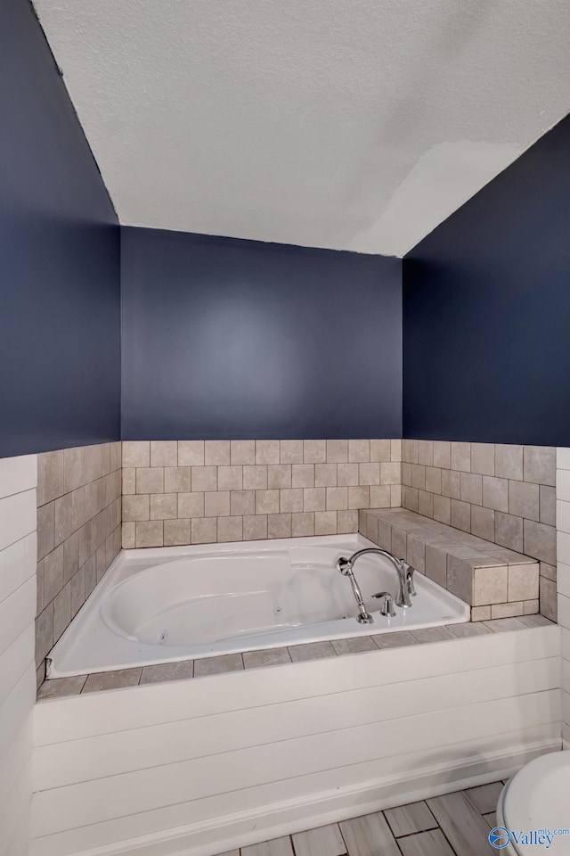 bathroom with hardwood / wood-style flooring, a relaxing tiled tub, a textured ceiling, and toilet