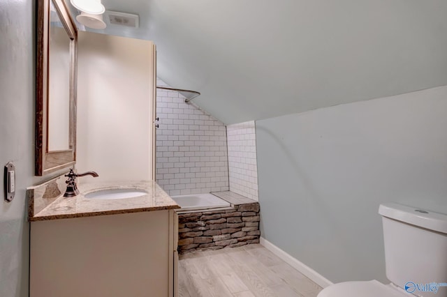 full bathroom with vanity, hardwood / wood-style flooring, toilet, tiled shower / bath, and lofted ceiling