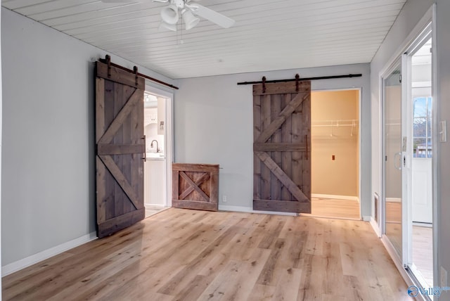 empty room with a barn door, ceiling fan, and light wood-type flooring