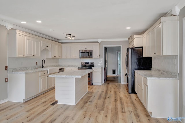 kitchen with crown molding, sink, light wood-type flooring, appliances with stainless steel finishes, and a kitchen island