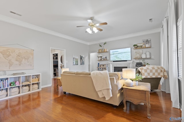 living room with a tile fireplace, hardwood / wood-style flooring, ceiling fan, and ornamental molding