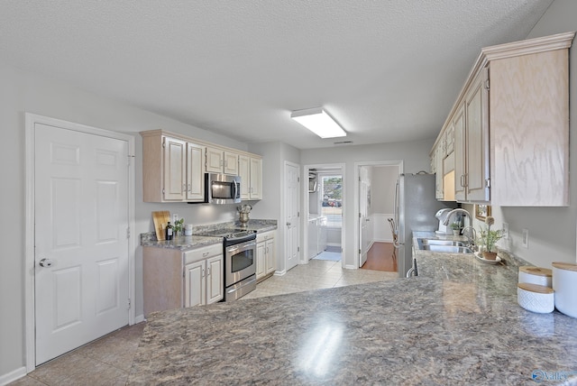 kitchen featuring sink, light tile patterned flooring, stainless steel appliances, and a textured ceiling