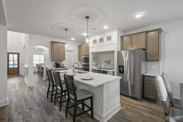 kitchen with stainless steel appliances, decorative backsplash, dark hardwood / wood-style flooring, decorative light fixtures, and a kitchen island with sink