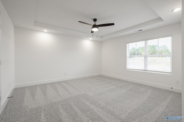 carpeted empty room with a raised ceiling and ceiling fan