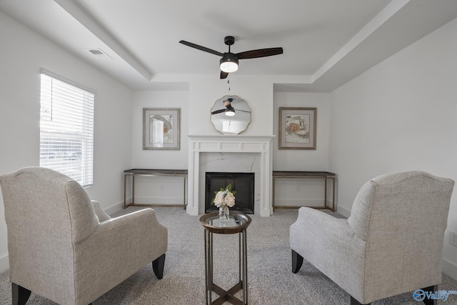 living room with a raised ceiling, ceiling fan, a fireplace, and light colored carpet