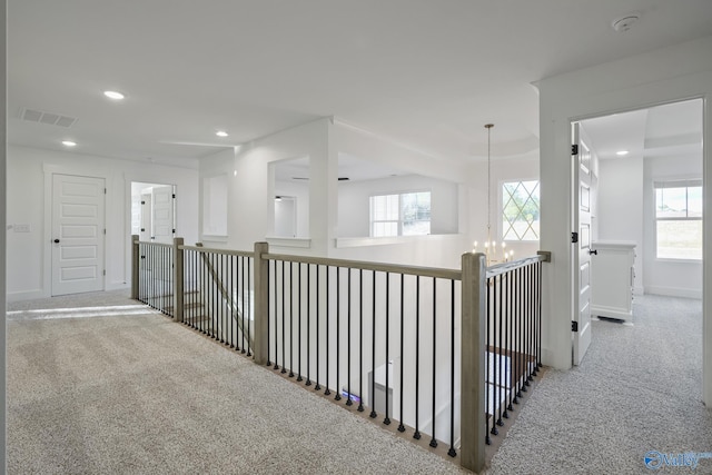 hall with a chandelier and light colored carpet