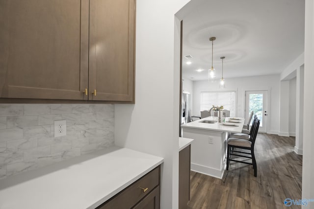 kitchen featuring sink, hanging light fixtures, a kitchen breakfast bar, an island with sink, and decorative backsplash