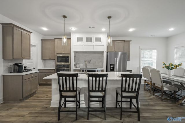 kitchen with appliances with stainless steel finishes, decorative light fixtures, tasteful backsplash, and a kitchen island with sink