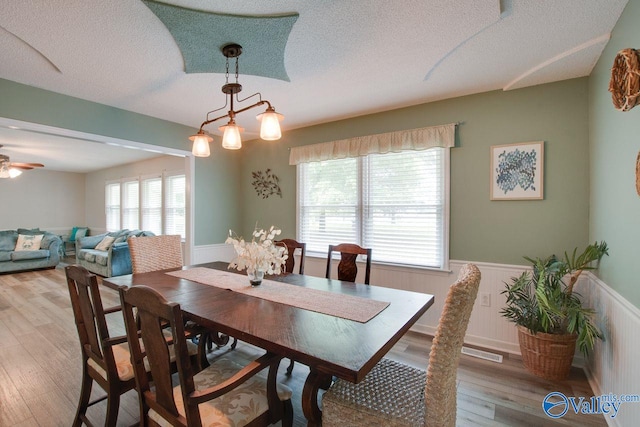 dining area with light wood-type flooring, ceiling fan with notable chandelier, and a wealth of natural light