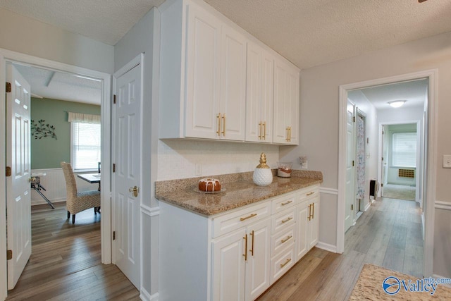 bar featuring light stone countertops, light hardwood / wood-style floors, white cabinetry, and a textured ceiling