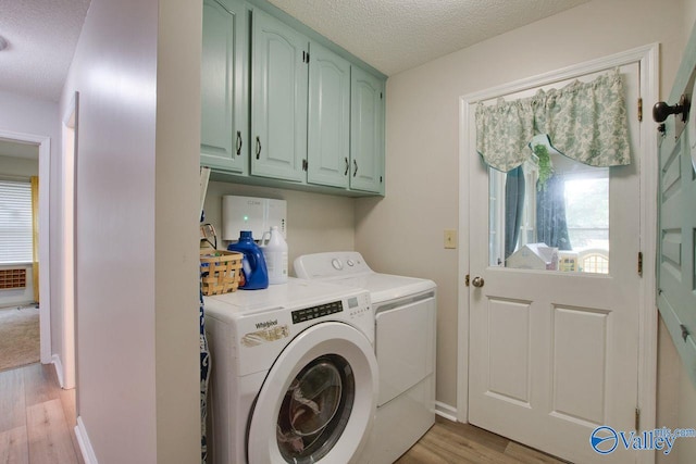 clothes washing area with light wood-type flooring, a textured ceiling, cabinets, and separate washer and dryer