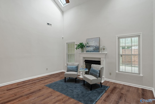 living area featuring a towering ceiling, dark wood-type flooring, and a skylight