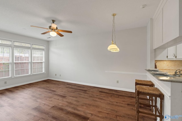 interior space with white cabinetry, ceiling fan, hanging light fixtures, dark wood-type flooring, and tasteful backsplash