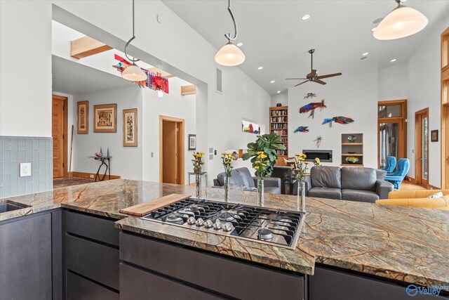 kitchen with dark stone countertops, decorative backsplash, decorative light fixtures, and stainless steel gas cooktop