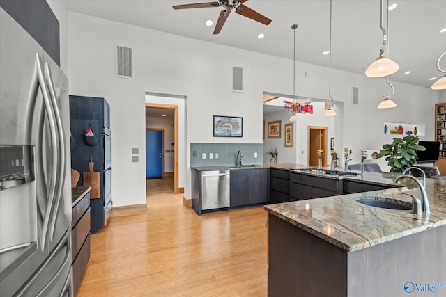 kitchen featuring sink, stainless steel appliances, a high ceiling, kitchen peninsula, and decorative light fixtures