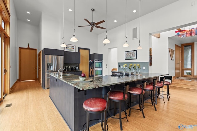 kitchen with a kitchen breakfast bar, light wood-type flooring, a towering ceiling, pendant lighting, and dark stone countertops