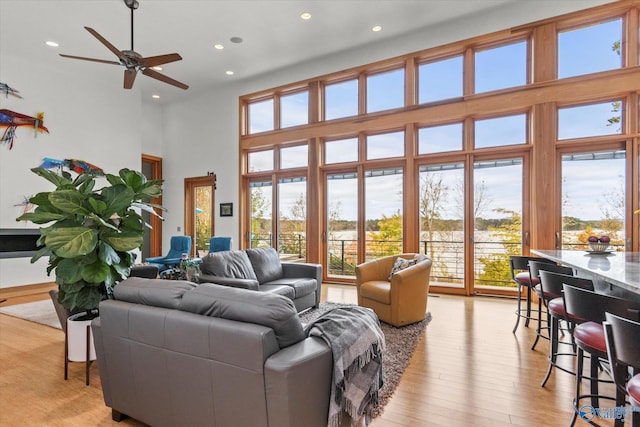 living room featuring ceiling fan, a towering ceiling, and light hardwood / wood-style floors