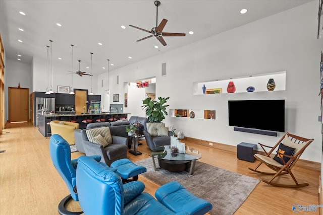 living room with ceiling fan, light wood-type flooring, and a towering ceiling