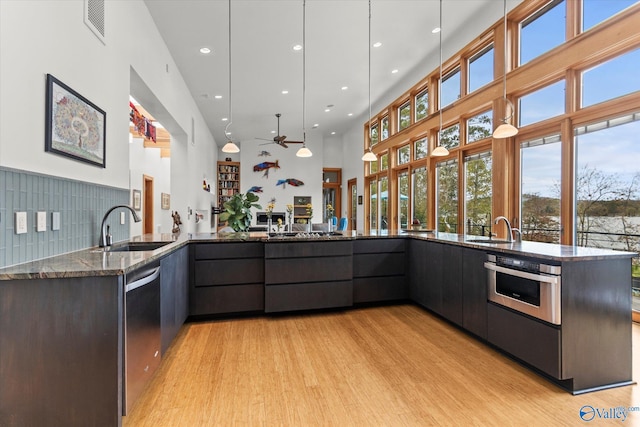 kitchen featuring light wood-type flooring, stainless steel appliances, ceiling fan, sink, and dark stone countertops