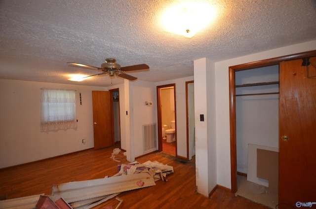 unfurnished bedroom featuring visible vents, a textured ceiling, wood finished floors, connected bathroom, and baseboards