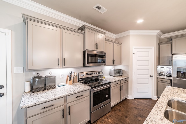 kitchen with gray cabinetry, light stone counters, dark hardwood / wood-style floors, appliances with stainless steel finishes, and ornamental molding