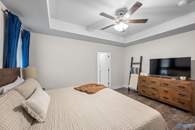 bedroom featuring dark hardwood / wood-style floors, ceiling fan, and a tray ceiling