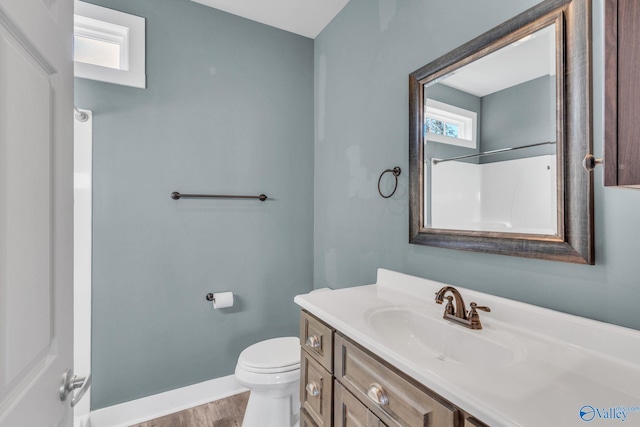 bathroom with toilet, vanity, wood finished floors, baseboards, and walk in shower