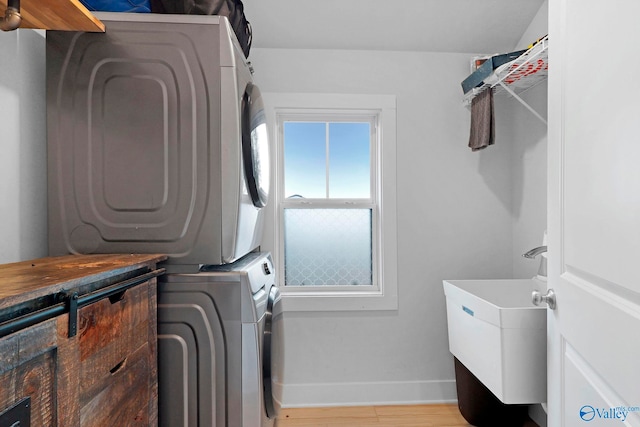 laundry room featuring laundry area, stacked washer / dryer, a sink, wood finished floors, and baseboards