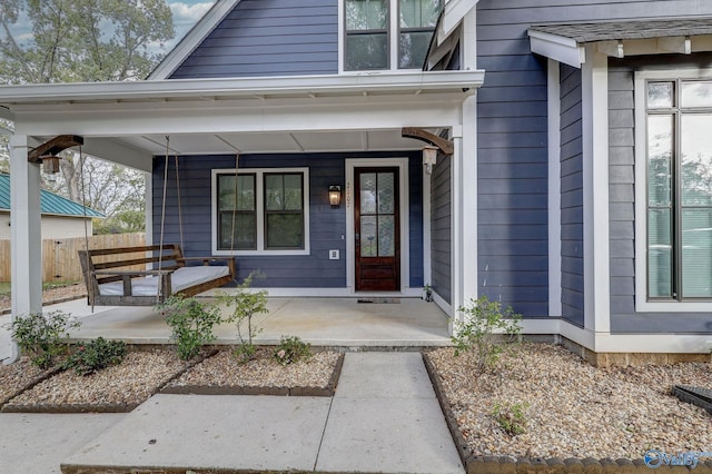 view of exterior entry with fence and a porch