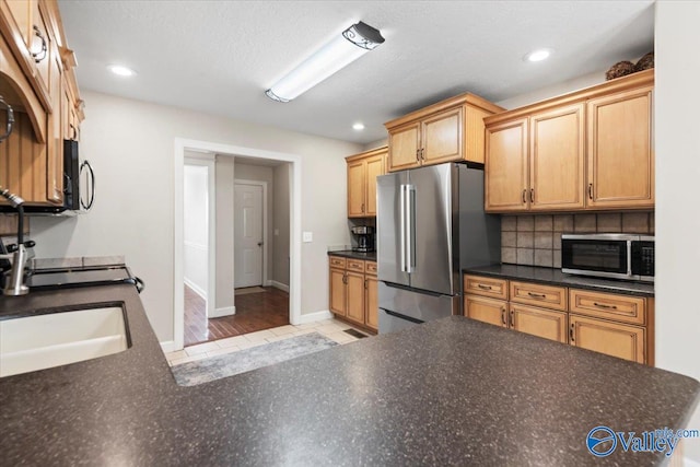 kitchen with sink, tasteful backsplash, light hardwood / wood-style flooring, a textured ceiling, and appliances with stainless steel finishes