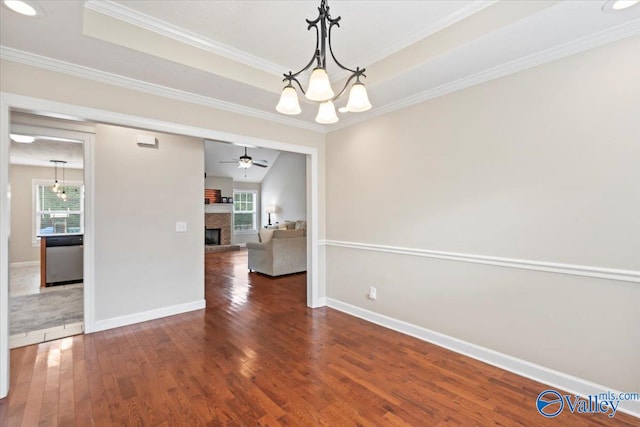 unfurnished dining area with a tray ceiling, ceiling fan with notable chandelier, dark hardwood / wood-style floors, and ornamental molding