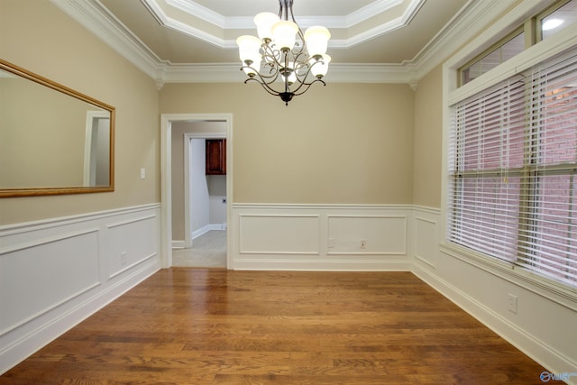 spare room featuring an inviting chandelier, a raised ceiling, ornamental molding, and wood finished floors